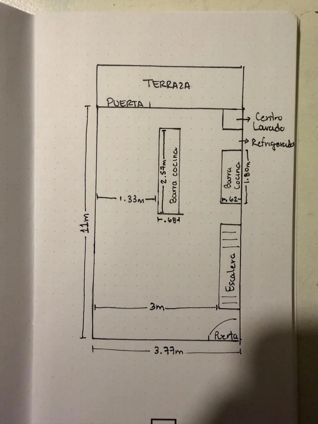 A phone photo of a ground-floor sketch drawn in pen on a dot-grid notebook page, with handwritten Spanish labels and dimension lines.